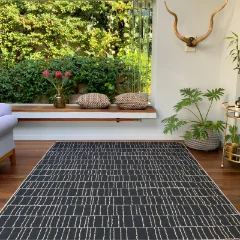 Dark Stacks outdoor rug on a covered stoep with a bench and potted plants
