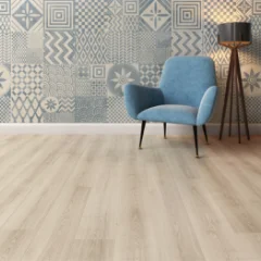 Ashen Oak laminate flooring meeting a patterned tile floor, with a blue armchair and floor lamp