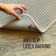 A hand lifting the corner of the Hill n Dale Stone rug to show its anti-slip latex backing