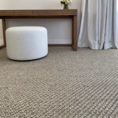 Sisal Heather carpet fitted in a bedroom beside a round white pouffe and a dark console