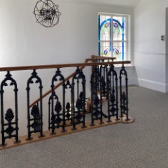 Veld Knotted Pewter carpet on a landing beside an ornate wrought-iron balustrade and arched window